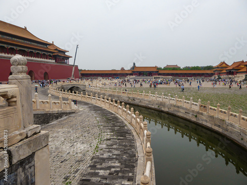 Inside of Forbidden City in Beijing, China. The building complex consist of many parts. There is a small canal in the middle of a square. Many people visiting the touristic spot. Air pollution.