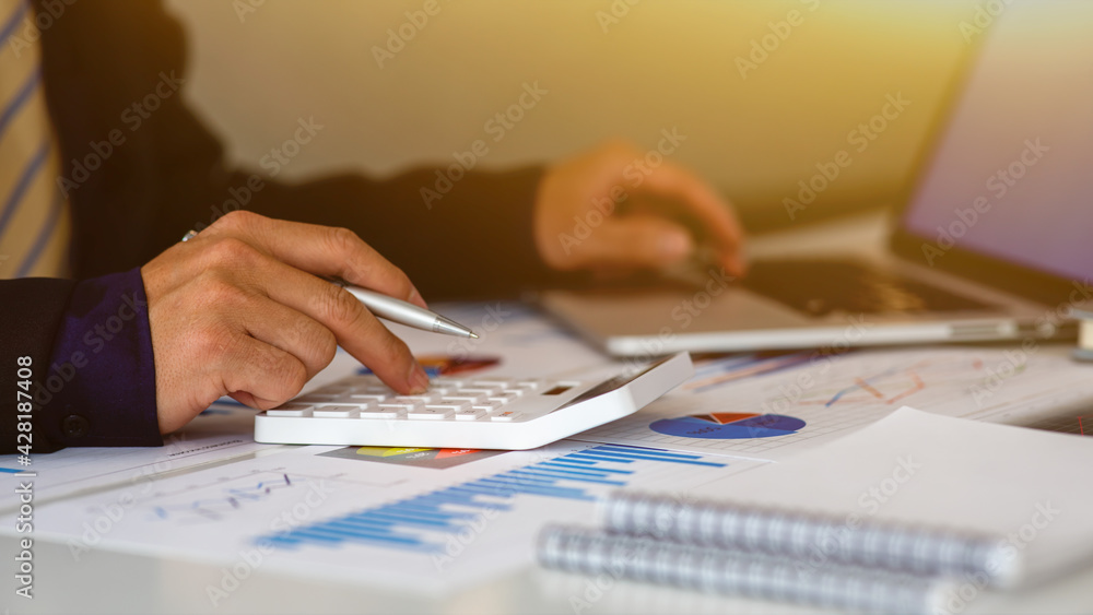 Close up Business man using calculator and laptop for do math finance on wooden desk, tax, accounting, statistics and analytical research concept Close up Business man using calculator and laptop for do math finance on wooden desk, tax, accounting, statistics and analytical research concept