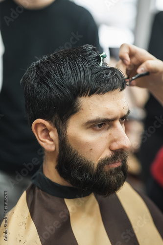 Salon barbershop man.Bearded man getting haircut by hairdresser and sitting in chair at barbershop. Bearded man or hipster. Fine Cuts. Portrait bearded man.
