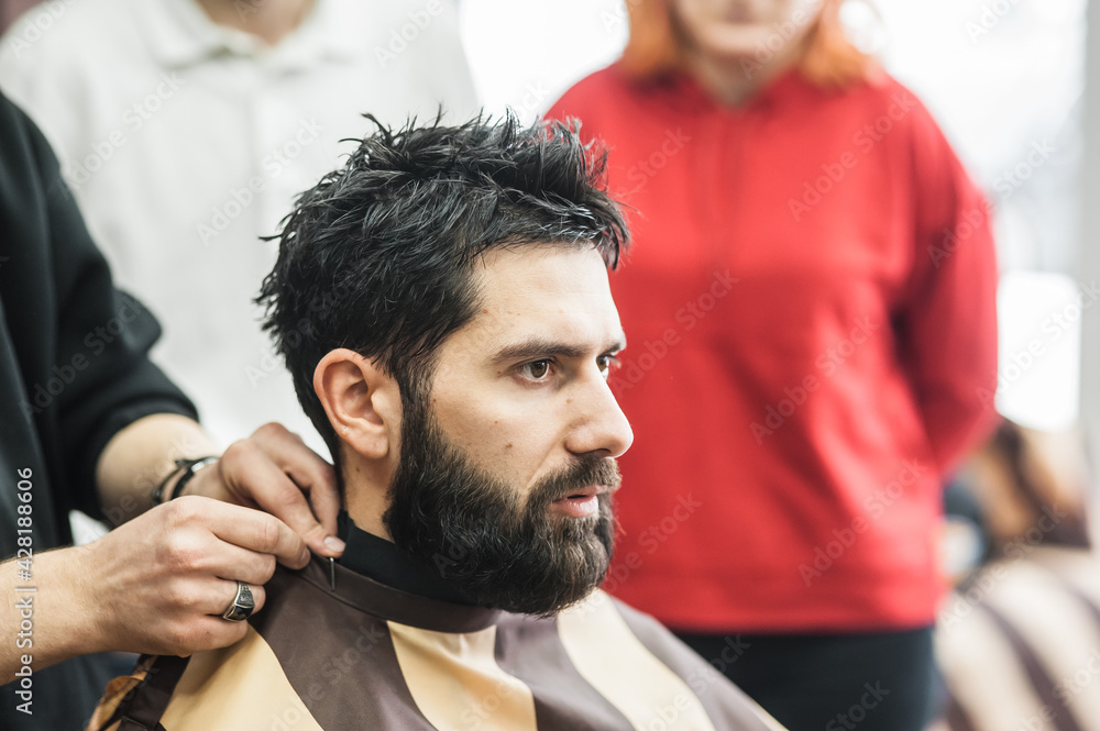 a hairdresser cuts a bearded young guy with a hair trimmer, combing the hair on his head. Work of the master in men's haircut in a barbershop a hairdresser cuts a bearded young guy with a hair trimmer, combing the hair on his head. Work of the master in men's haircut in a barbershop