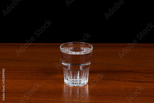 There is a shot of vodka on a wooden surface.