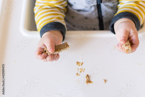 Toddler hands holding strips of bread with peanut butter on them; early exposure to allergenic foods baby led weaning