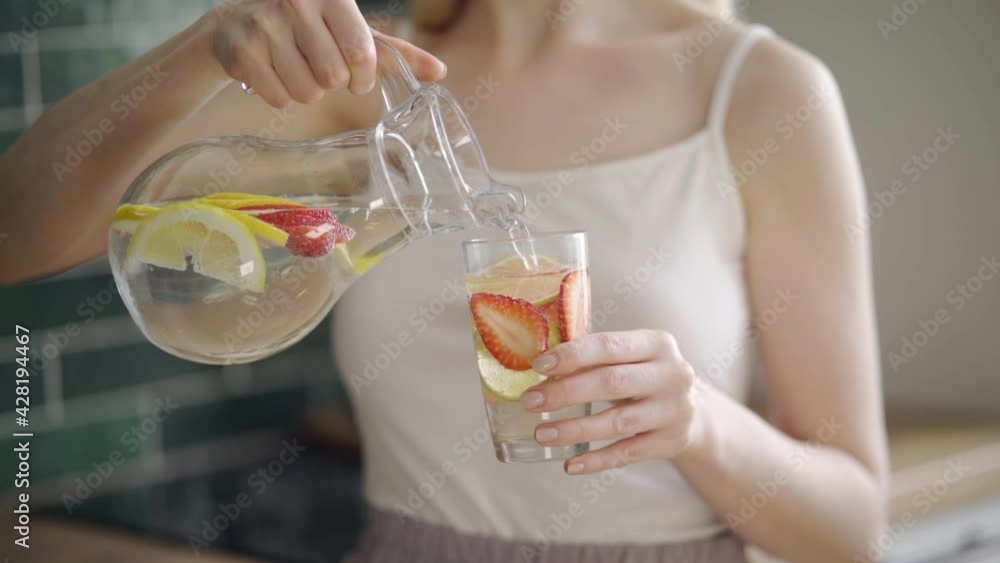 young woman mixes delicious refreshing drink with lemon and strawberry slices in glass jug on light blurred background slow motion young woman mixes delicious refreshing drink with lemon and strawberry slices in glass jug on light blurred background slow motion