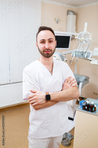 Dentist at the workplace. Cheerful bearded doctor in a spacious modern office and looking at the camera with a kind smile
