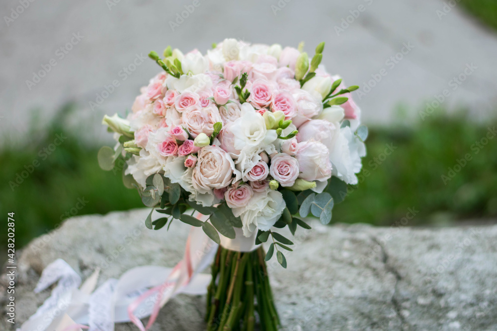 Beautiful bridal bouquet of white and pink flowers and greenery, decorated with long silk ribbon lies on a gray textural background. Beautiful bridal bouquet of white and pink flowers and greenery, decorated with long silk ribbon lies on a gray textural background.