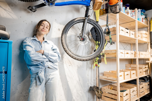 Portrait of a young handywoman standing relaxed in the workshop or garage with bicycle and wooden shelves