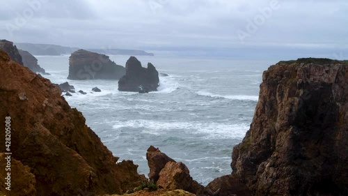 Scenic view of the coastline along Carrapateira with the rock formations and waves crashing in the rocks during a storm, in Algarve, Portugal