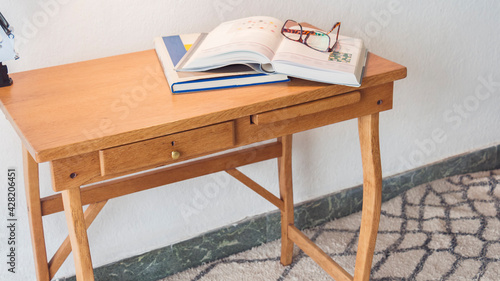 Tiny desk made of wood with books and glasses to read over it isolated in a bright and white apartment. An office established at home to keep on working remotely