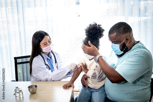 African American father using his hand covering his daughter's eyes which is scared, while the woman doctor was vaccinated against the flu virus. to people health care and vaccine concept.