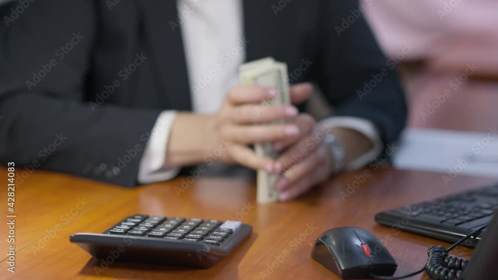 Close-up of calculator on office table with blurred female hands counting money at background. Unrecognizable wealthy businesswoman calculating dollars at workplace indoors. Success and richness Close-up of calculator on office table with blurred female hands counting money at background. Unrecognizable wealthy businesswoman calculating dollars at workplace indoors. Success and richness