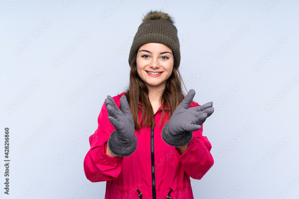 Young girl with winter hat isolated on blue background applauding after presentation in a conference Young girl with winter hat isolated on blue background applauding after presentation in a conference