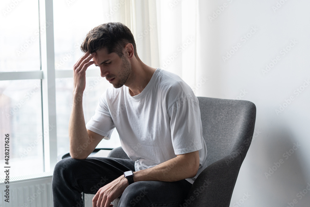 Depressed lonely man having a headache siting in an empty room