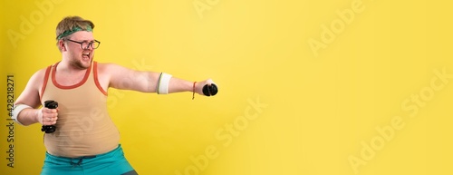 Funny fat man in sportswear with dumbbells in his hands. Overweight man goes in for sports. Yellow background isolate