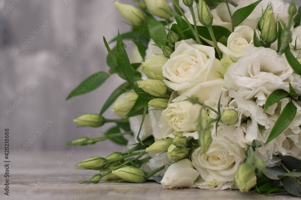 Fototapeta premium Beautiful bridal bouquet of white flowers and greenery, decorated with long silk ribbon lies on a gray textural background. Copy space