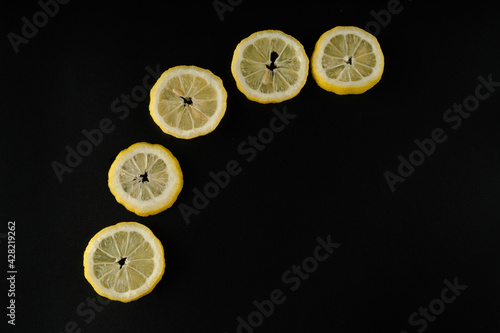Five lemon slices lined up in a semicircle on a black background isolated