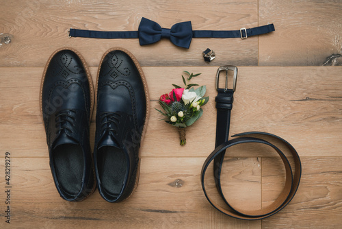 Wedding fashion for men. Top view of boutonniere, shoes, cufflinks, leather belt and bow tie on wooden background.