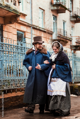 A man and a woman, elegantly dressed, in 19th-century clothes, walk and talk