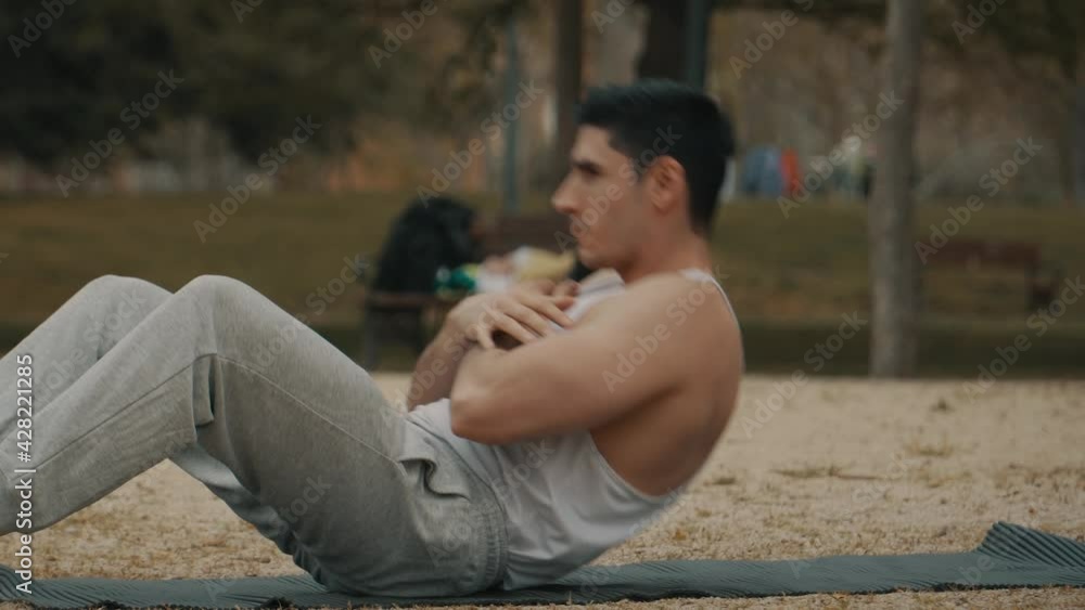 Hombre musculoso haciendo ejercicio abdominal, hombre con camiseta de tirantes blanca y chándal gris haciendo ejercicio, hombre de pelo corto entrenando en el parque, quemando grasa abdominal