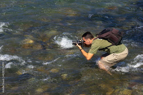 A nature photographer explores a mountain river in shallow water in search of unusual shots of photography from different angles.