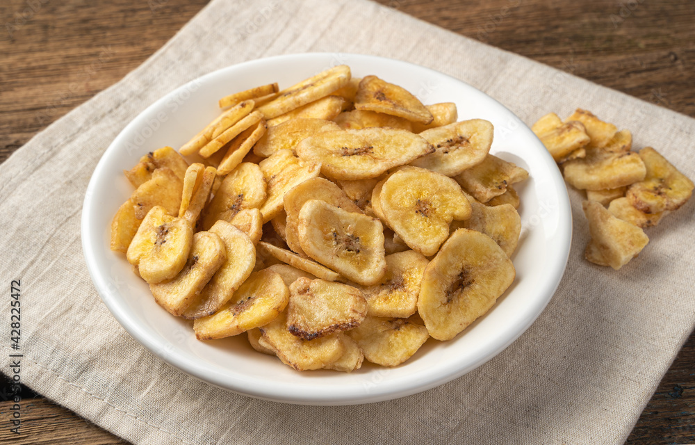 Banana chips in a white plate on a linen napkin. Side view.