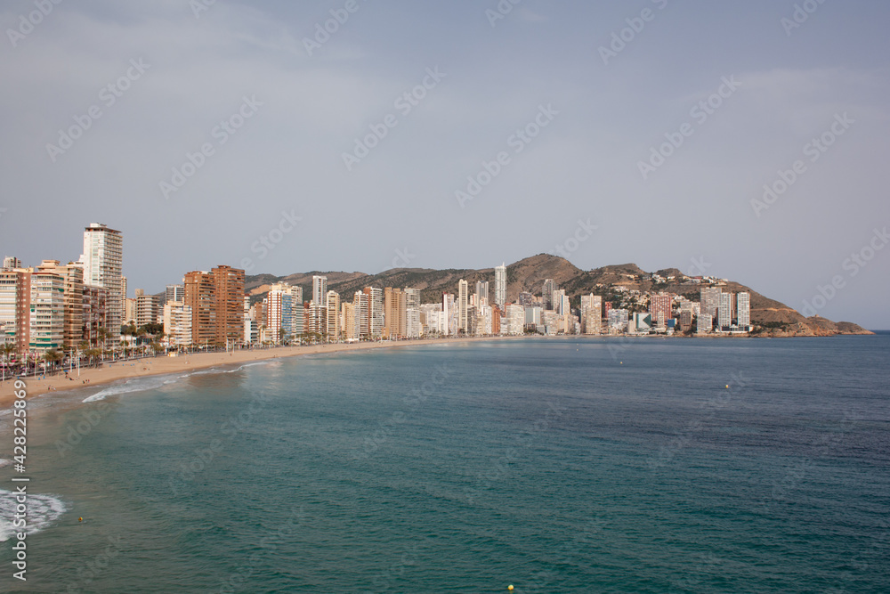 View of the Mediterranean sea without waves, the Levante beach and the skyline of Benidorm on the Alicante coast with the mountains in the background.