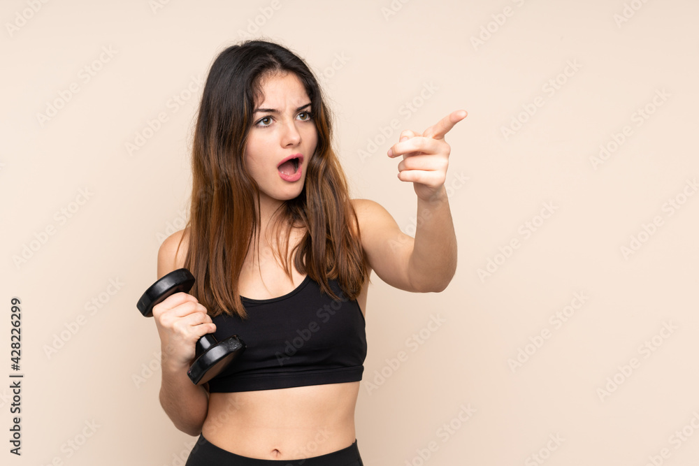 Young sport woman making weightlifting isolated on beige background pointing away Young sport woman making weightlifting isolated on beige background pointing away