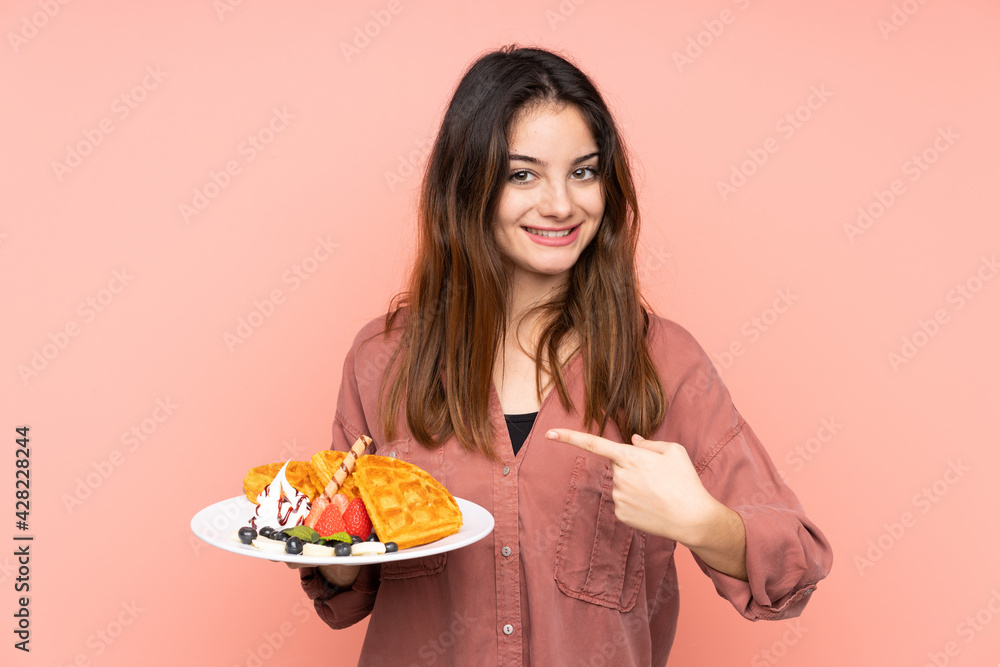 Young caucasian woman holding waffles isolated on pink background with surprise facial expression