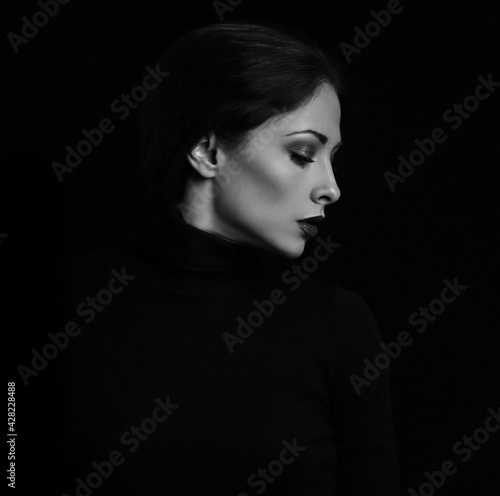 Sexy woman with bright evening makeup, red lipstick brown brow posing isolated on dark black background. Closeup portrait in deep low key light shadows. Art.