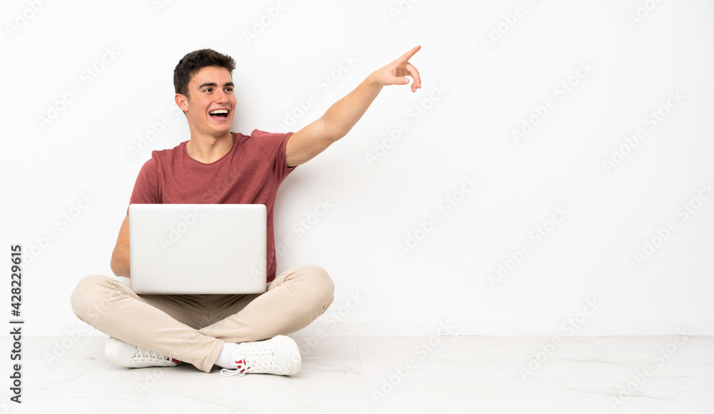 Teenager man sitting on the flor with his laptop pointing away Teenager man sitting on the flor with his laptop pointing away