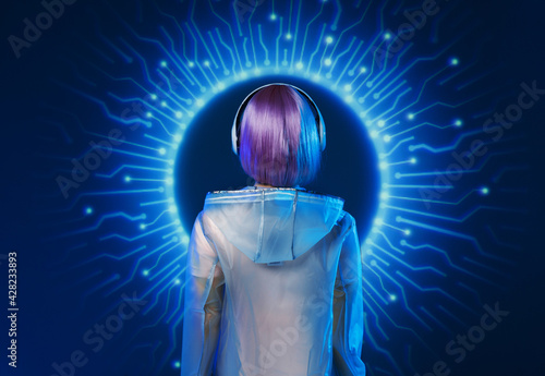 Beautiful woman with purple hair in futuristic costume. Blue and violet neon light. Young girl in modern headphones listening music. Futuristic holographic interface.