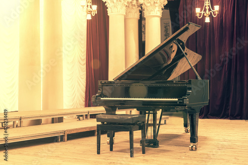 Grand Piano in Concert Hall. Piano standing on empty stage. opened black grand piano with stool on a wooden concert stage. toned