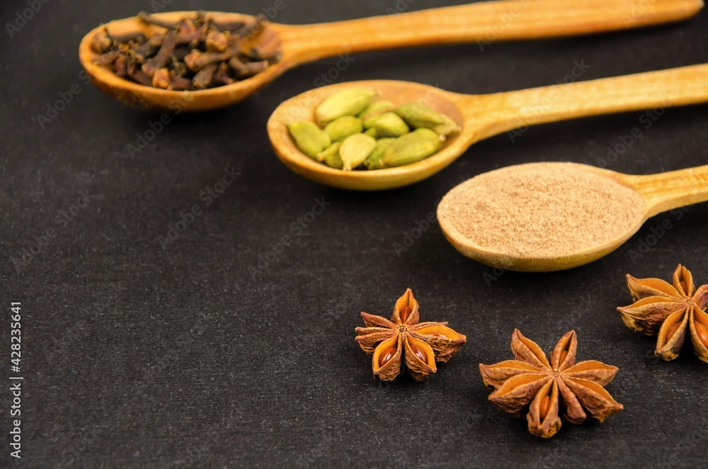 Various spices in wooden spoons and star anise on dark background