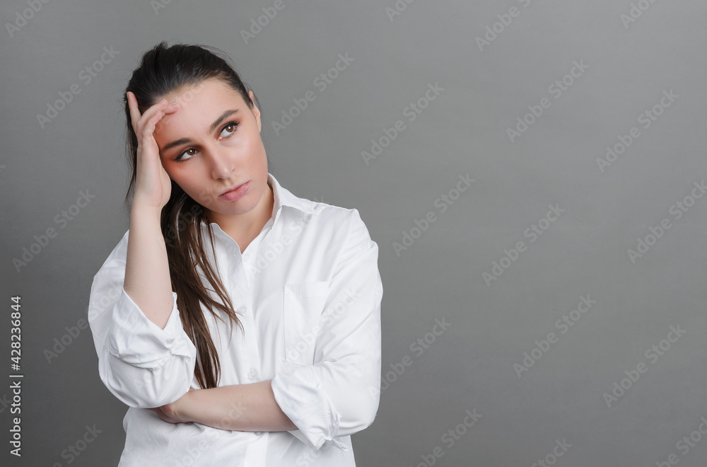 young woman in a white shirt tired, pensive on a gray background young woman in a white shirt tired, pensive on a gray background