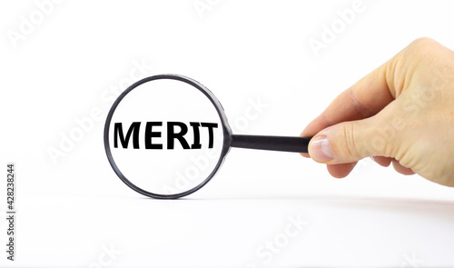 Merit symbol. Magnifying glass with word merit on a beautiful white background. Businessman hand. Business and merit concept, copy space.