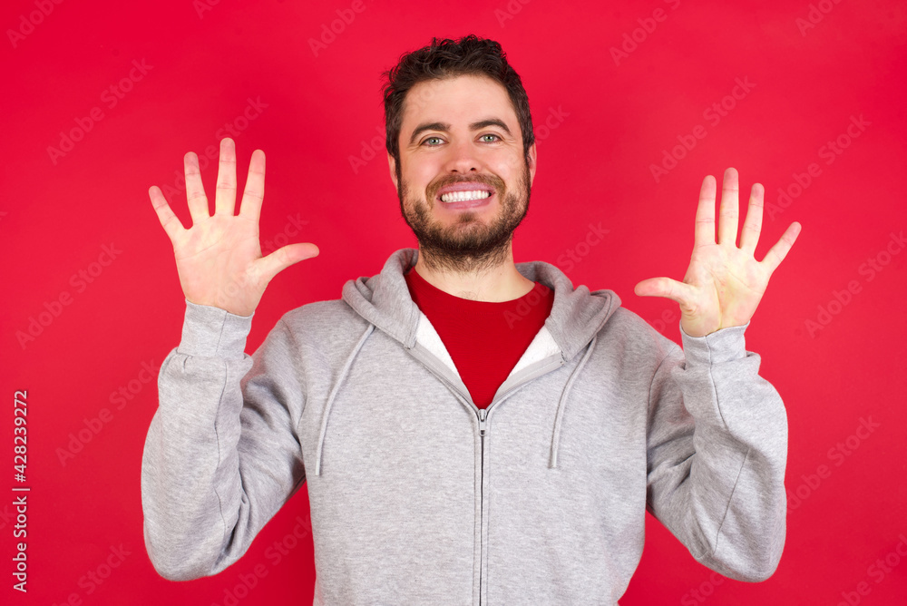 Young caucasian man wearing tracksuit over red background showing and pointing up with fingers number ten while smiling confident and happy. Young caucasian man wearing tracksuit over red background showing and pointing up with fingers number ten while smiling confident and happy.