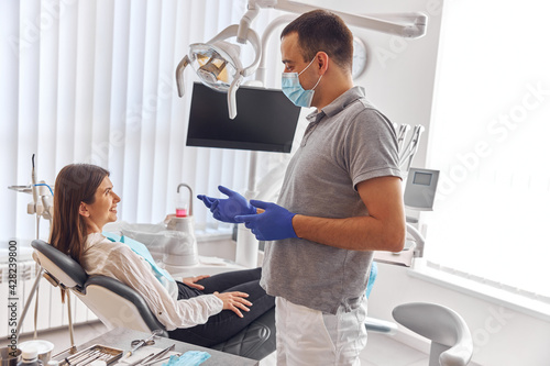 Cheerful positive dentist and client in dentistry. They look at each other and smile. Female client sit in chair