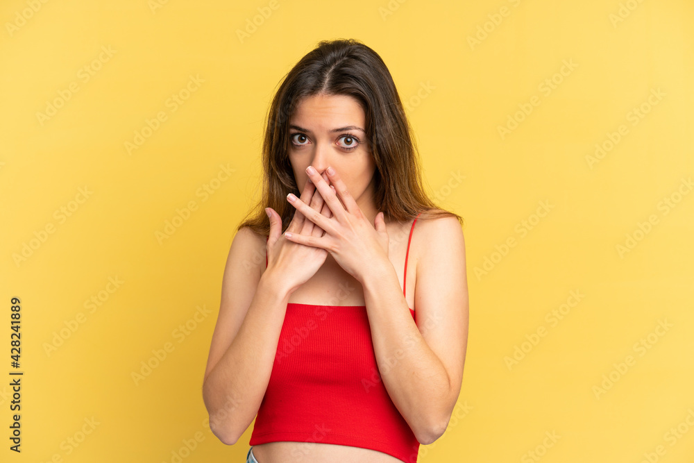 Young caucasian woman isolated on yellow background covering mouth with hands Young caucasian woman isolated on yellow background covering mouth with hands