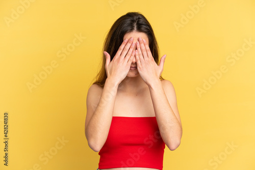 Young caucasian woman isolated on yellow background covering eyes by hands © luismolinero