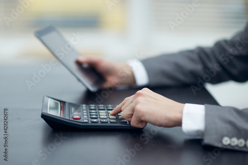 Manager holds a tablet in his left hand in his right hand works on a calculator