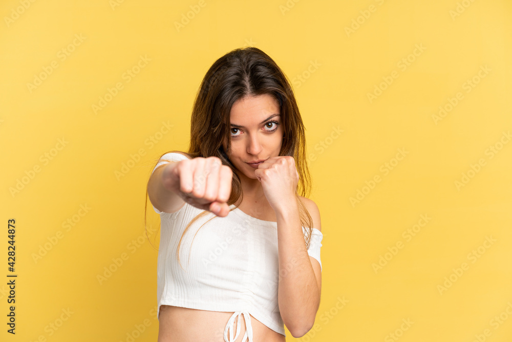 Young caucasian woman isolated on yellow background with fighting gesture Young caucasian woman isolated on yellow background with fighting gesture