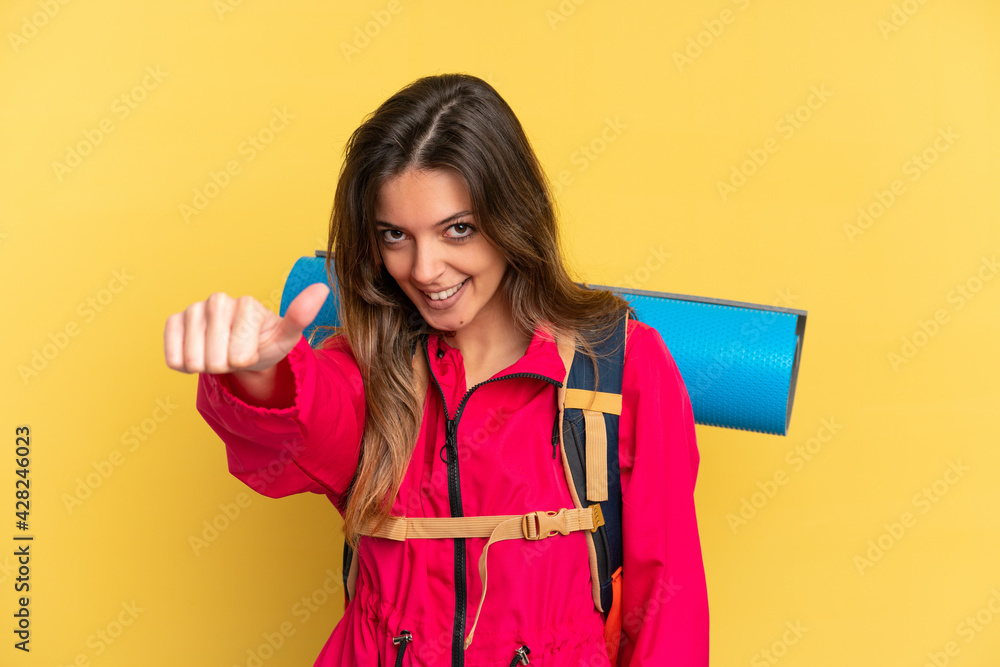 Young mountaineer man with a big backpack isolated on yellow background giving a thumbs up gesture Young mountaineer man with a big backpack isolated on yellow background giving a thumbs up gesture