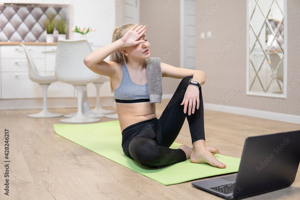 young attractive girl resting after fitness at home and looking at the laptop. quarantine fitness concept. High Quality young attractive girl resting after fitness at home and looking at the laptop. quarantine fitness concept. High Quality