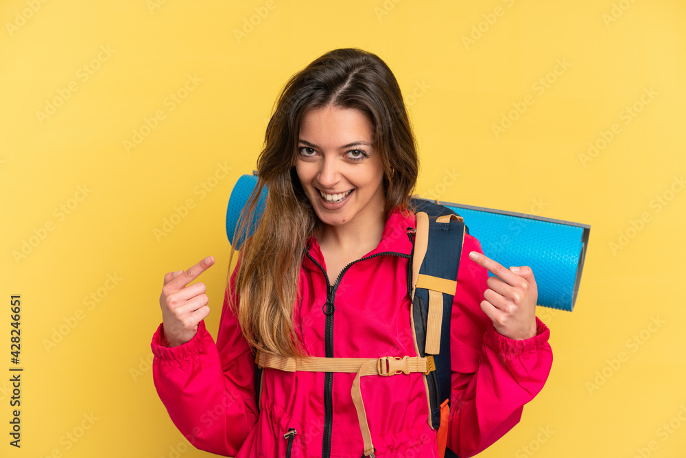 Young mountaineer man with a big backpack isolated on yellow background giving a thumbs up gesture Young mountaineer man with a big backpack isolated on yellow background giving a thumbs up gesture