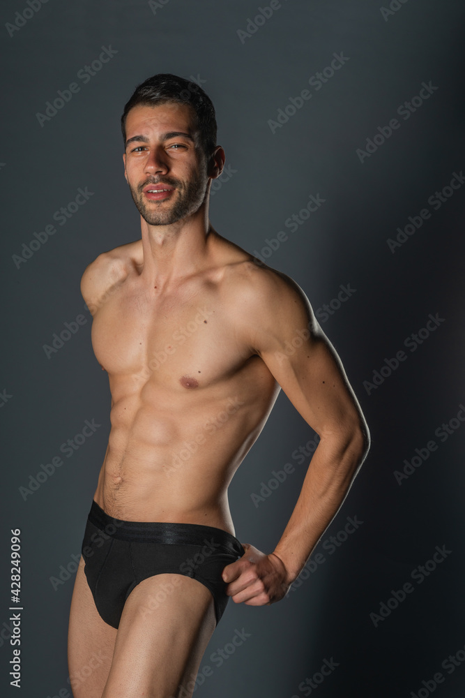 Fashion close-up portrait of a handsome male with bare torso posing in black underwear on isolated background