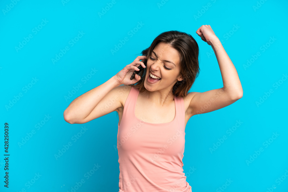 Young caucasian woman using mobile phone isolated on blue background celebrating a victory