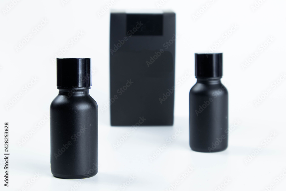 Glass bottle of hair care cream mixed with small black bamboo charcoal powder, placed on a white background. With a black packing box Glass bottle of hair care cream mixed with small black bamboo charcoal powder, placed on a white background. With a black packing box
