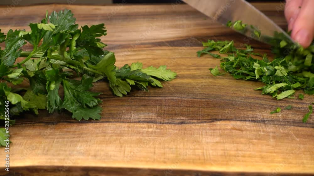 The cook cuts parsley on a wooden cutting board. The cook cuts parsley on a wooden cutting board.