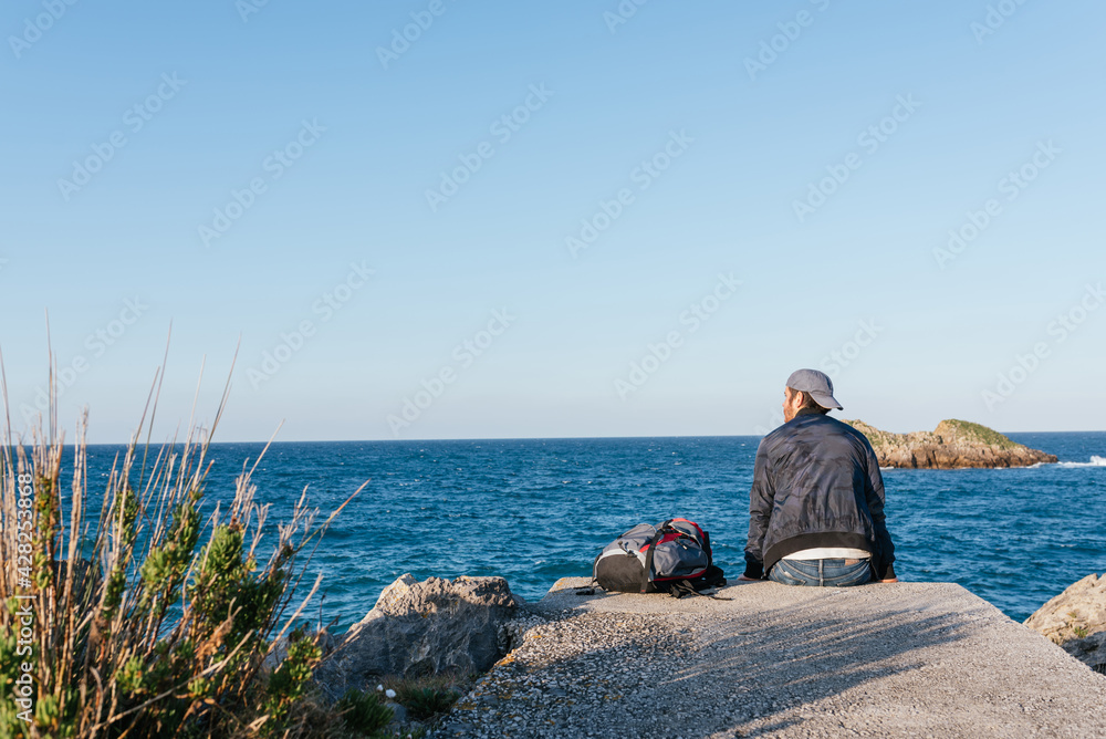 Traveler man sitting with his backpack in front of the sea. person meditating and thinking. nomad life