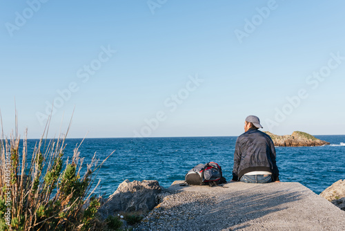 Traveler man sitting with his backpack in front of the sea. person meditating and thinking. nomad life