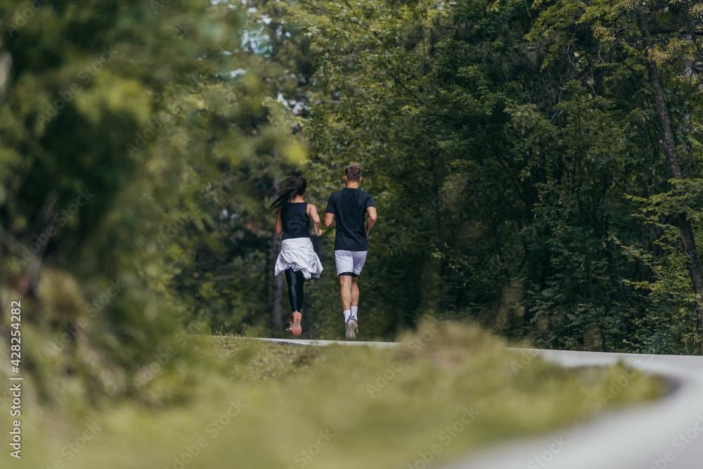 Young fit couple atheltes running on running road in a forest.